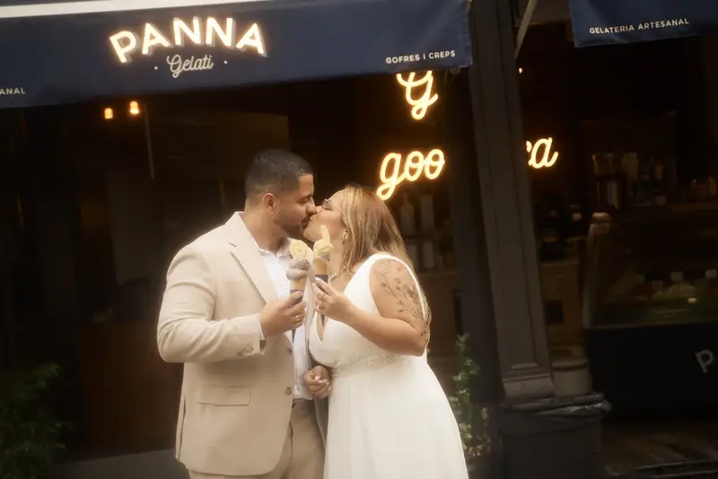 Gisele e Victor se beijando com casquinhas de sorvete na mão, sob um letreiro de neon amarelo