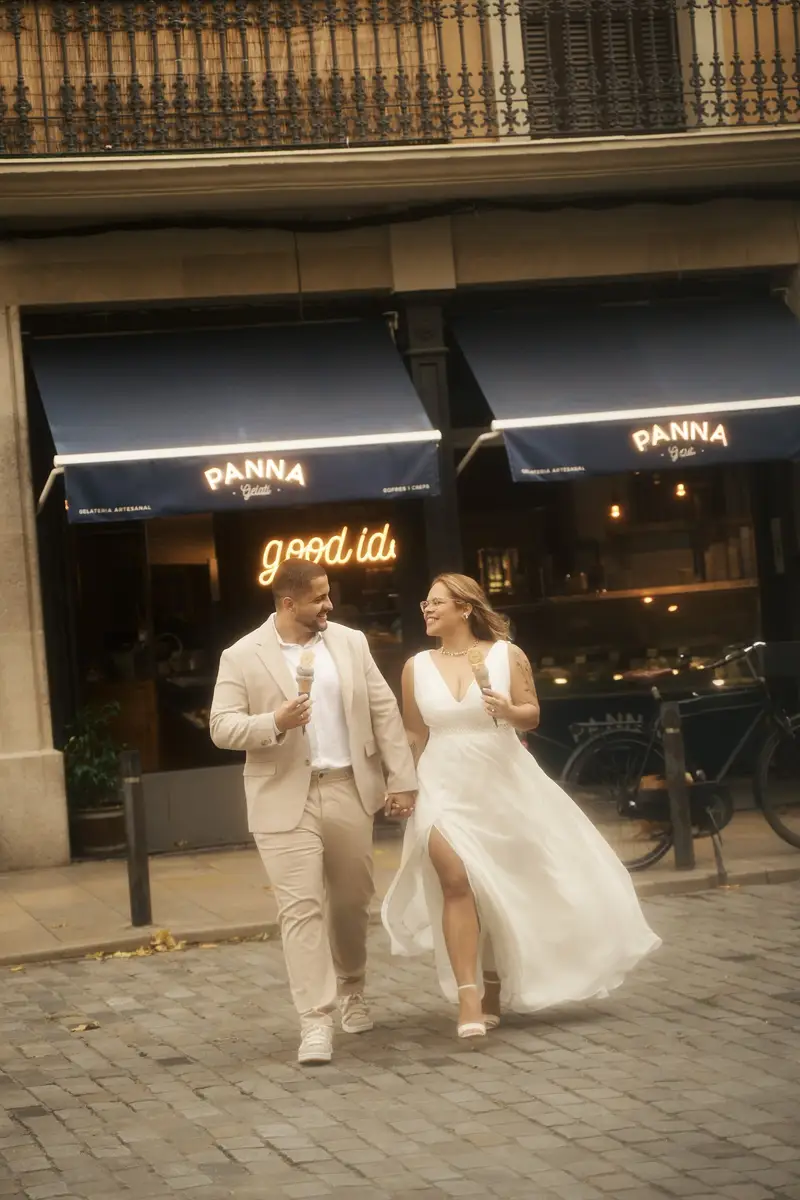 O casal caminhando e rindo com os sorvetes, em frente a uma sorveteria com toldos escuros